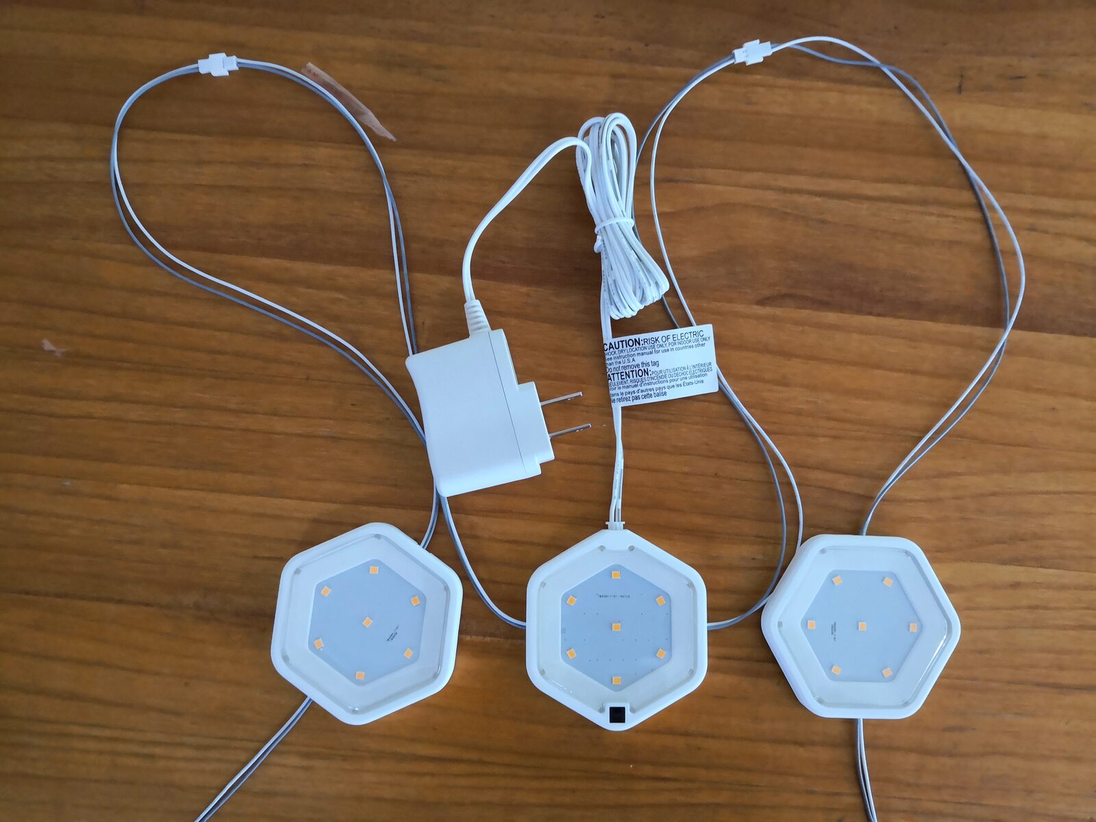 Three white hexagonal lights connected by thin wires to a white power adapter on a wooden table.