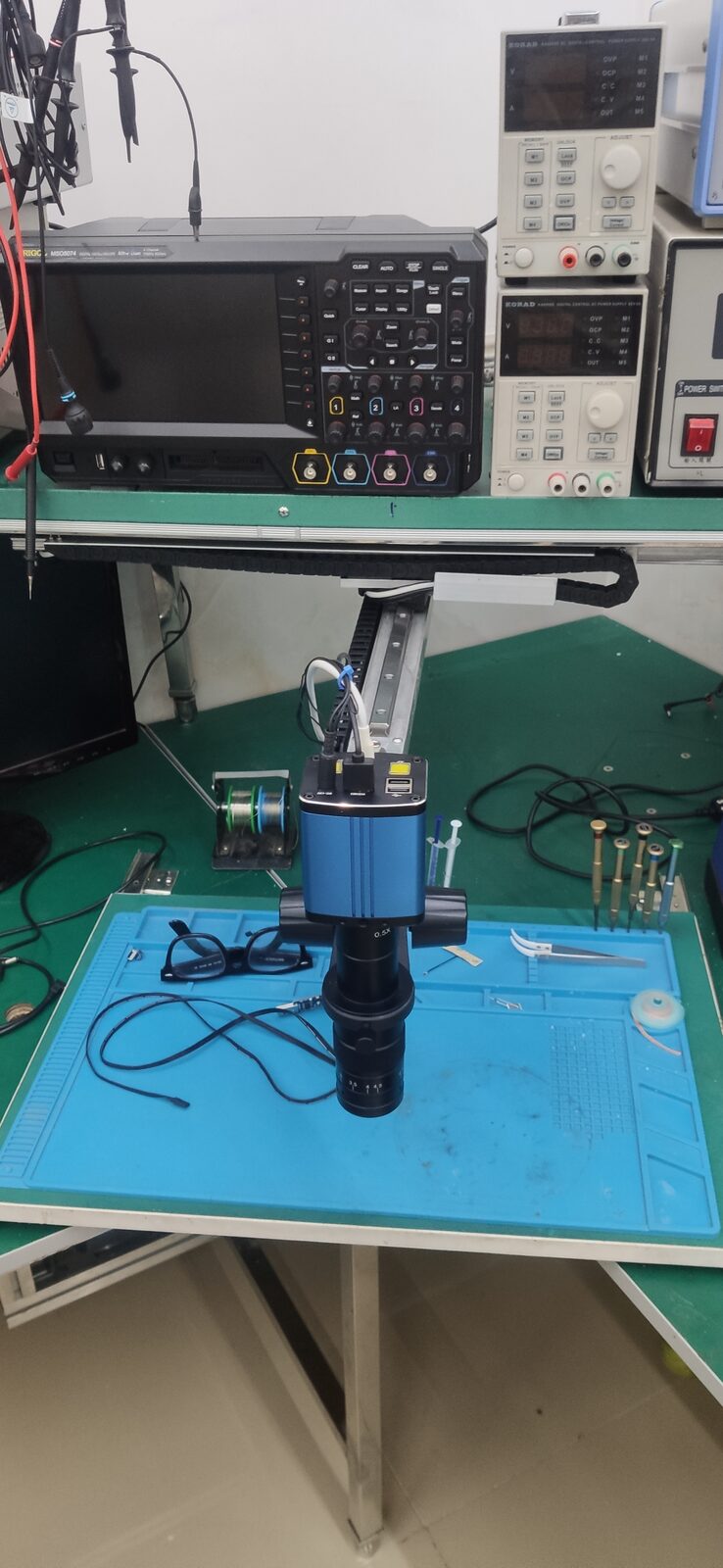 Close view of the blue digital microscope hanging over the blue work mat, with a rail arm above it.