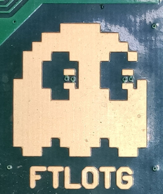 Close-up of a cream-coloured copper pixel-art ghost on a dark green board, with FTLOTG below.