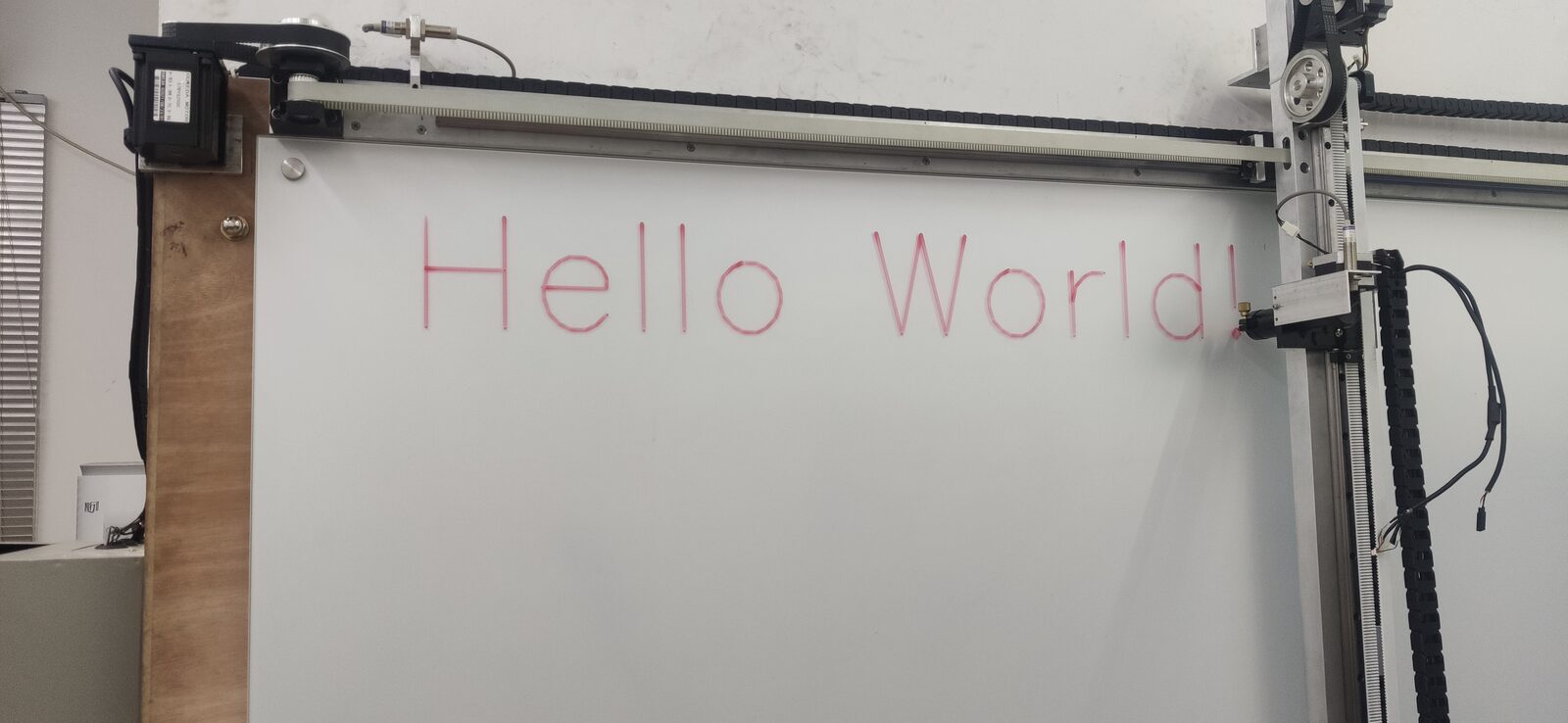 Whiteboard in a wooden frame with the word 'Hello World' written in light pink by the plotter.