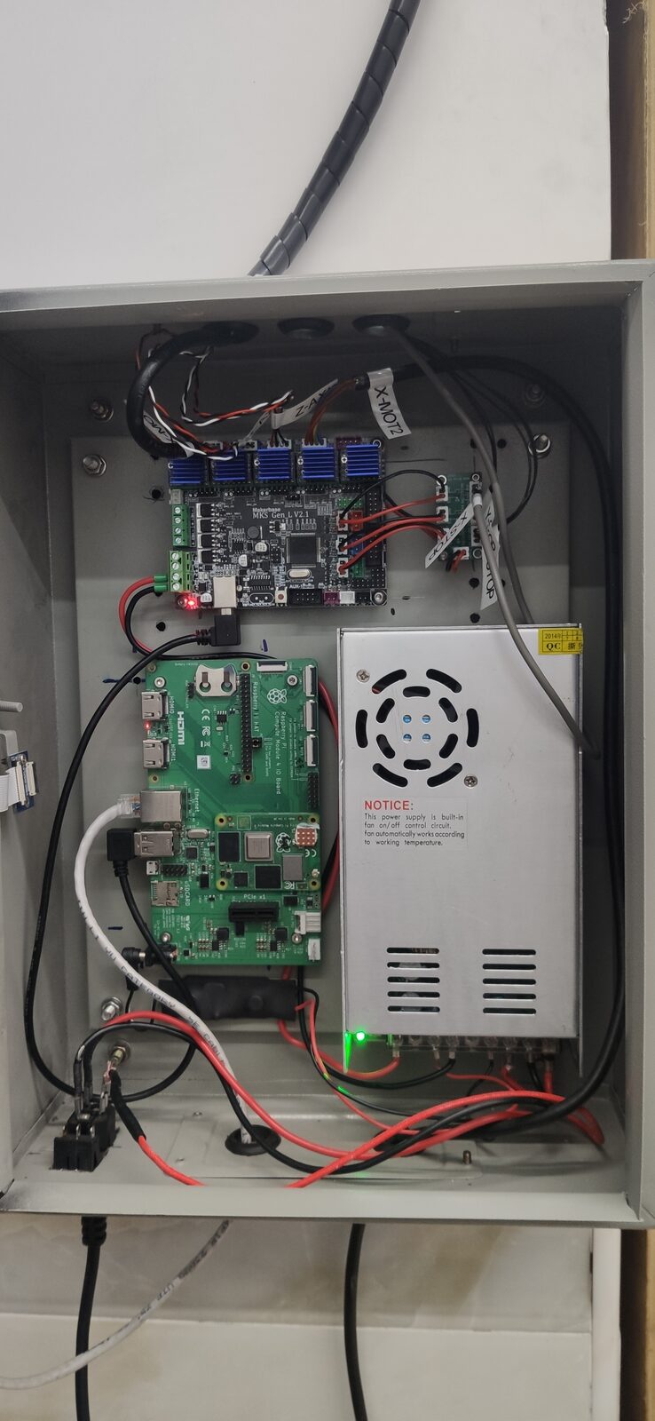 Open grey electronics enclosure holding a green circuit board, a ventilated power supply and wiring.